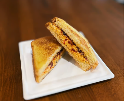 Grilled sandwich with a golden crust and cheese filling, cut diagonally, served on a square white plate on a wooden table. Cozy and inviting tone.